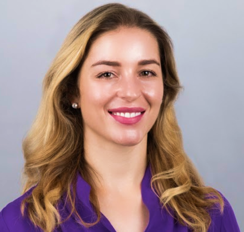 A headshot of a smiling woman with blonde hair and a purple button down shirt.